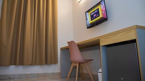 Une chambre moderne équipée d’un bureau, d’une chaise, d’un téléviseur fixé au mur et d’une fenêtre avec des rideaux.