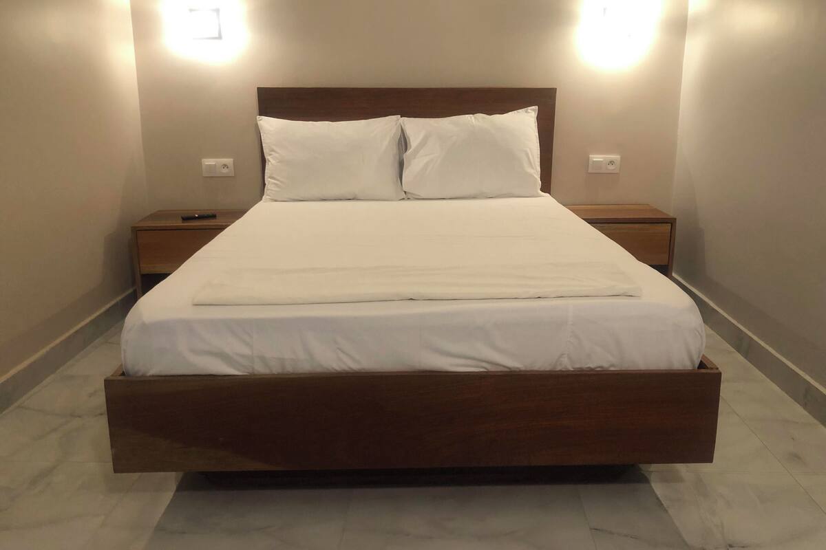 A neatly made bed with a wooden headboard, two bedside tables, and wall-mounted lights.