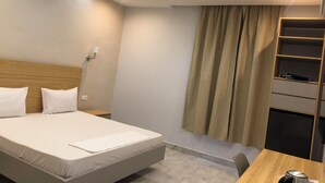 Une chambre d’hôtel comprenant un lit, des tables de chevet, un bureau, une chaise, une étagère avec des objets et un rideau.