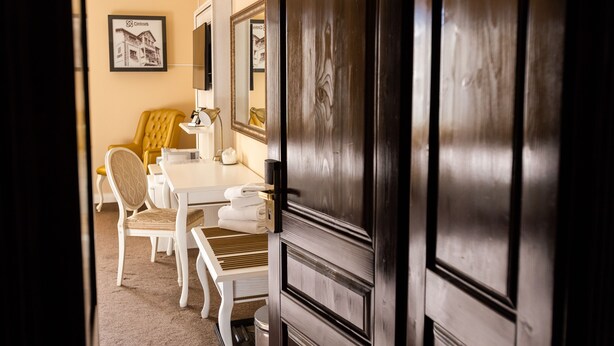 Habitación de hotel con comedor, puerta de madera, un cuadro en la pared y una mesa blanca con sillas.