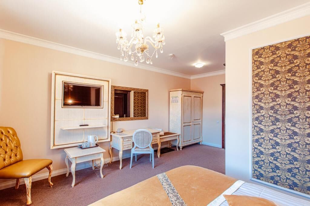 A bedroom with a bed, a desk, a chair, a wardrobe, and a chandelier.