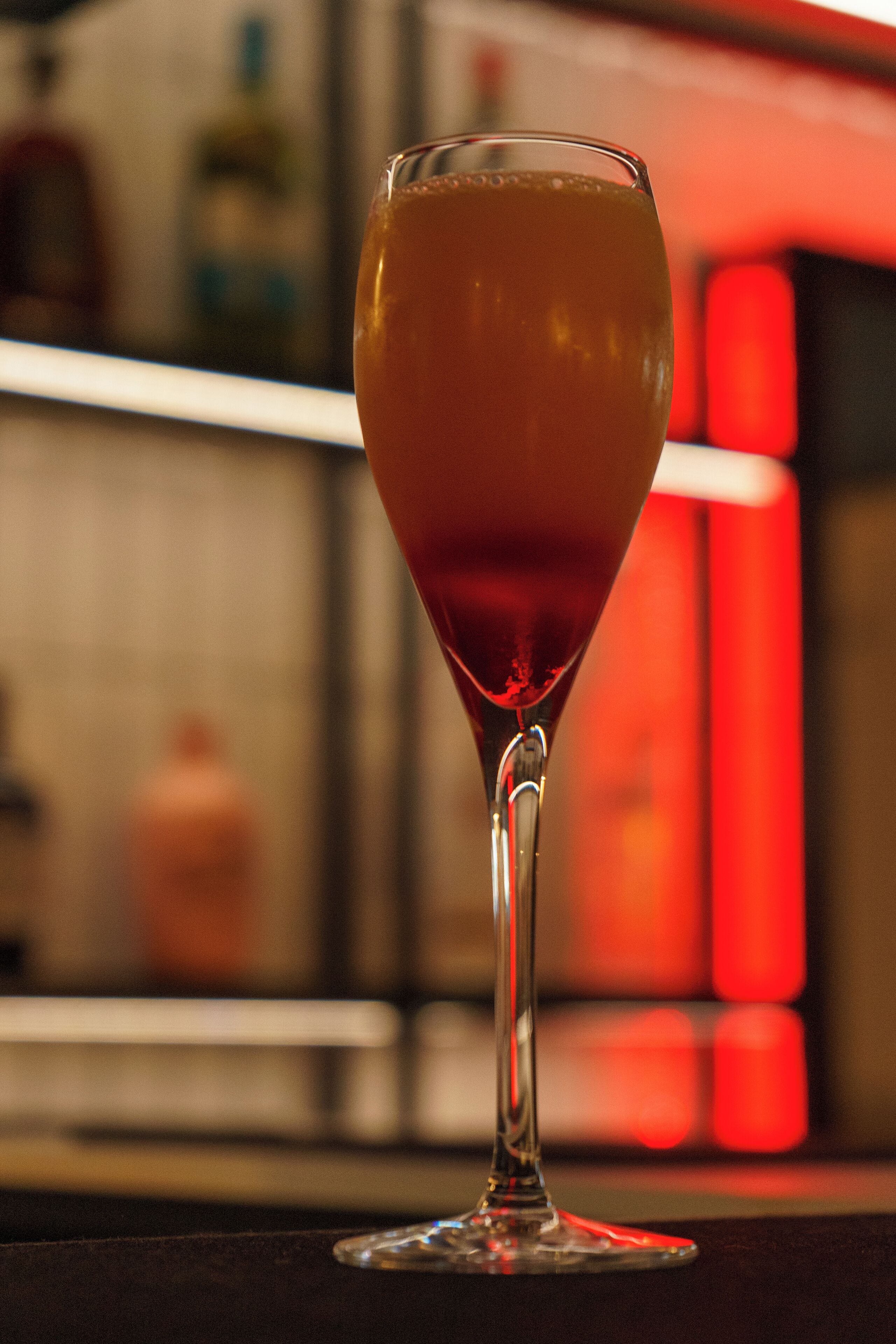 A glass of red wine on a bar counter with a blurred background.