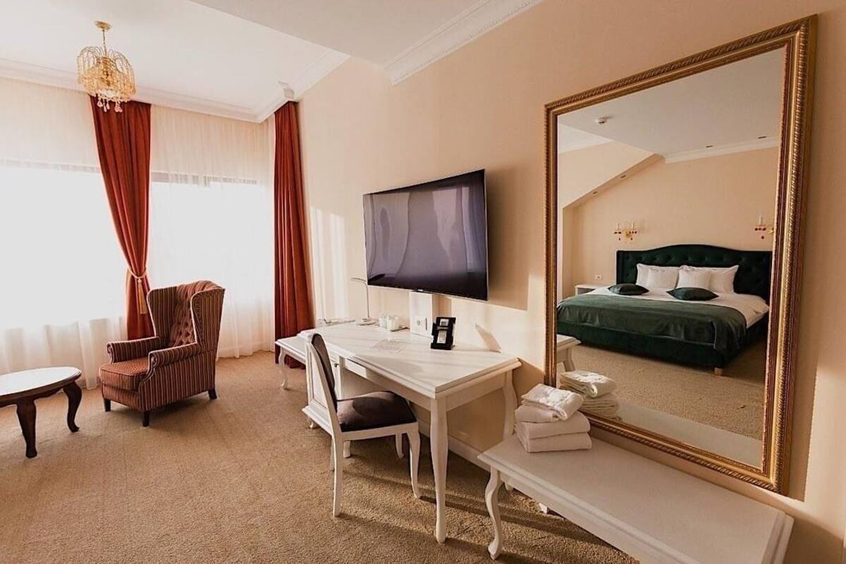 A hotel room with a large bed, a television, a desk with a chair, and a mirror.