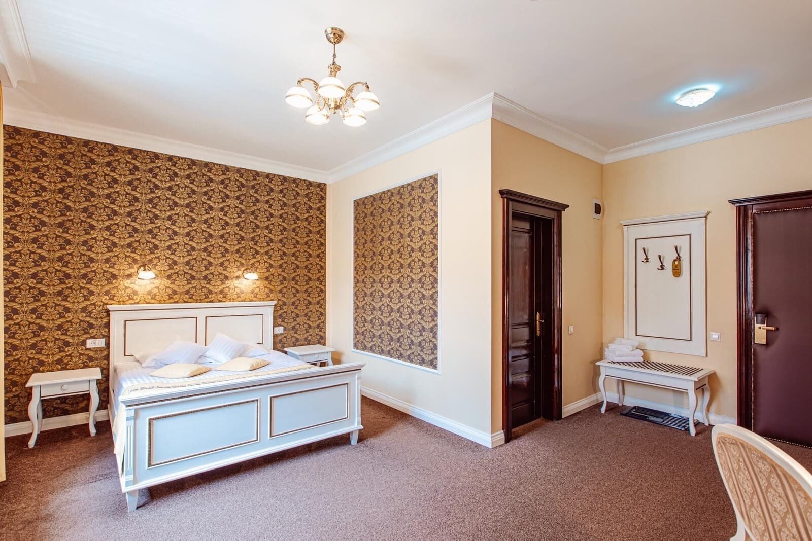 A bedroom with a large bed, a bedside table, a wardrobe, a mirror, and a chandelier.
