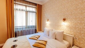 Una habitación de hotel con una cama grande, dos lámparas de noche, un ventanal con cortinas y papel tapiz estampado.