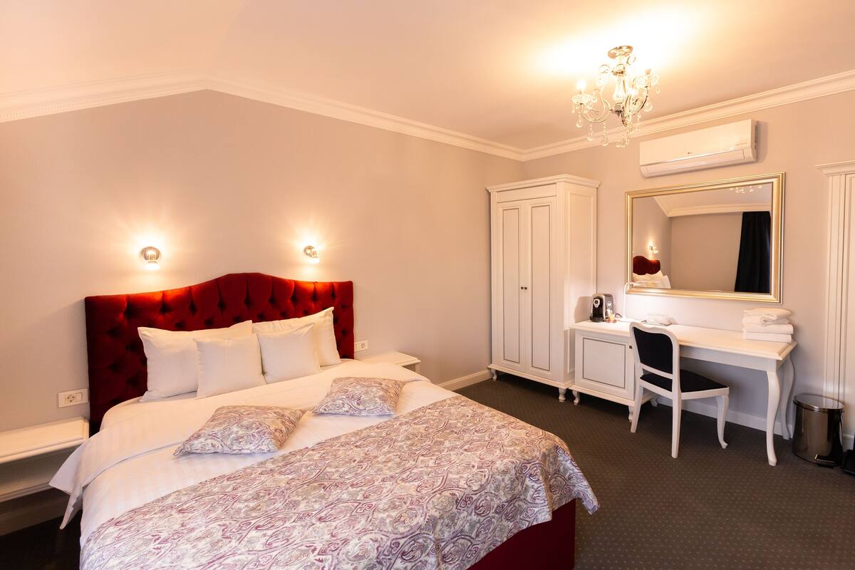 A bedroom with a large bed, a desk, a chair, and a wardrobe.