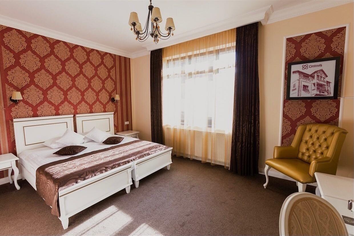 A hotel room with a large bed, a chair, a nightstand, and a chandelier.