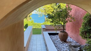 A view through an arched structure with a potted plant, a pathway, and a glimpse of a blue body of water in the background. - Apartment in a residence on the shores of Lake Garda (Pai)