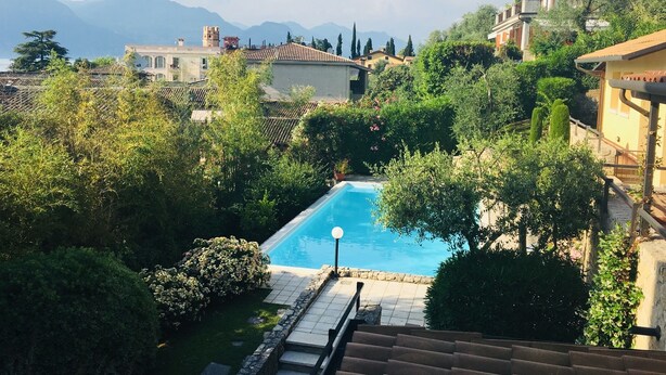 A swimming pool surrounded by lush greenery and a mountainous backdrop. - Apartment in a residence on the shores of Lake Garda (Pai)