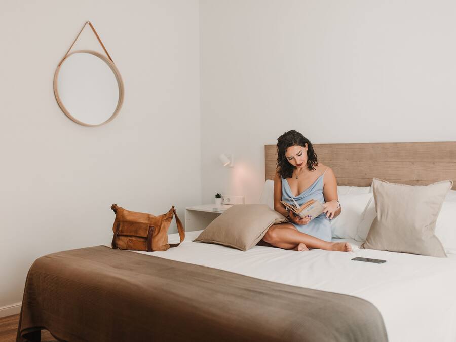 Una cama con cabecera de madera, una bolsa marrón, una almohada y un teléfono inteligente sobre la cama.