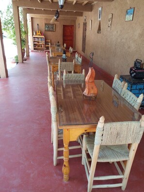 A long dining table with woven chairs, a guitar, and bookshelves in the background. - Maison Nomades (Asrir)