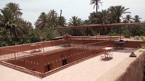 Un patio con un espacio central abierto, rodeado de palmeras y una valla de metal rojo.