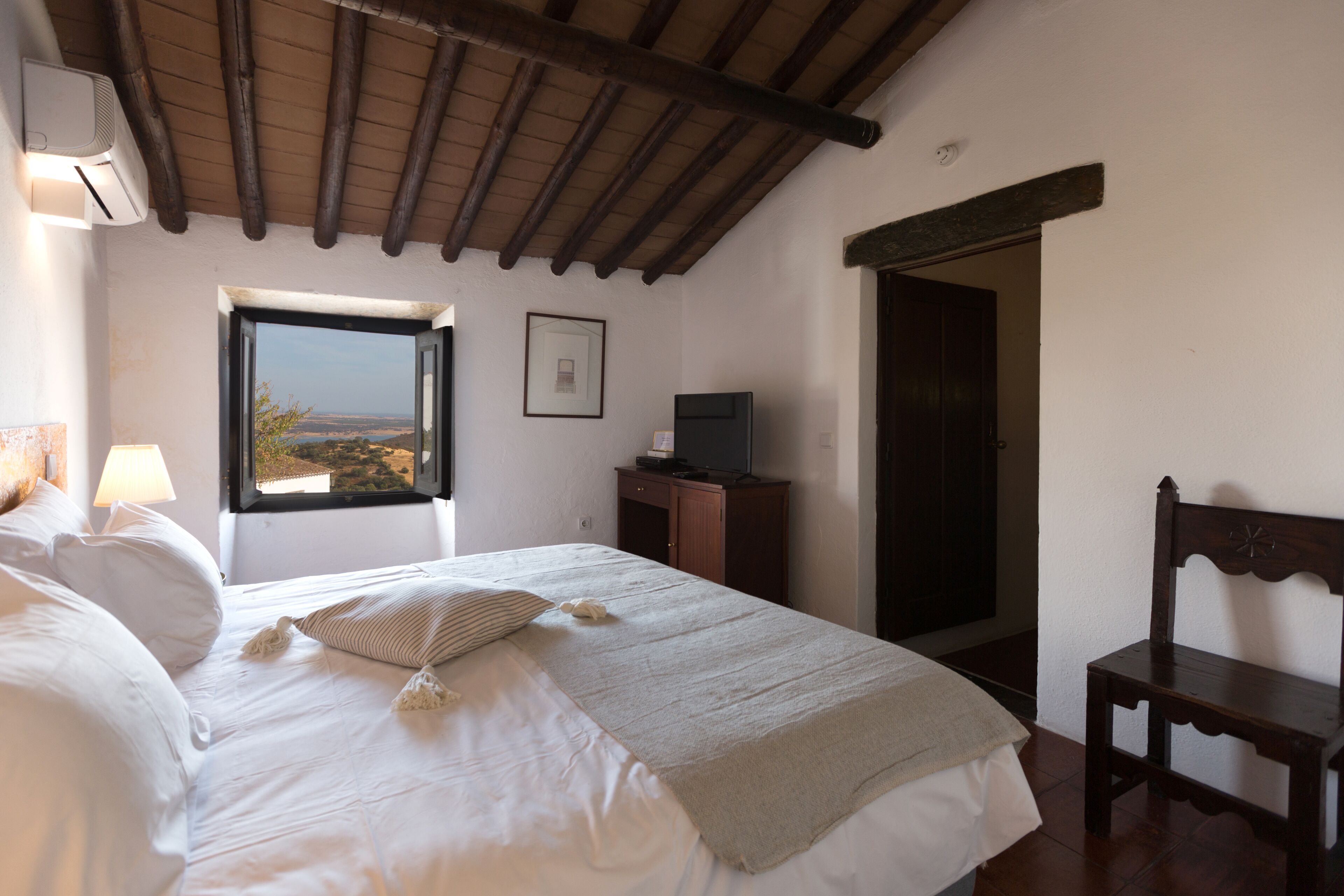 A bedroom with a bed, a window, a television, and a chair.