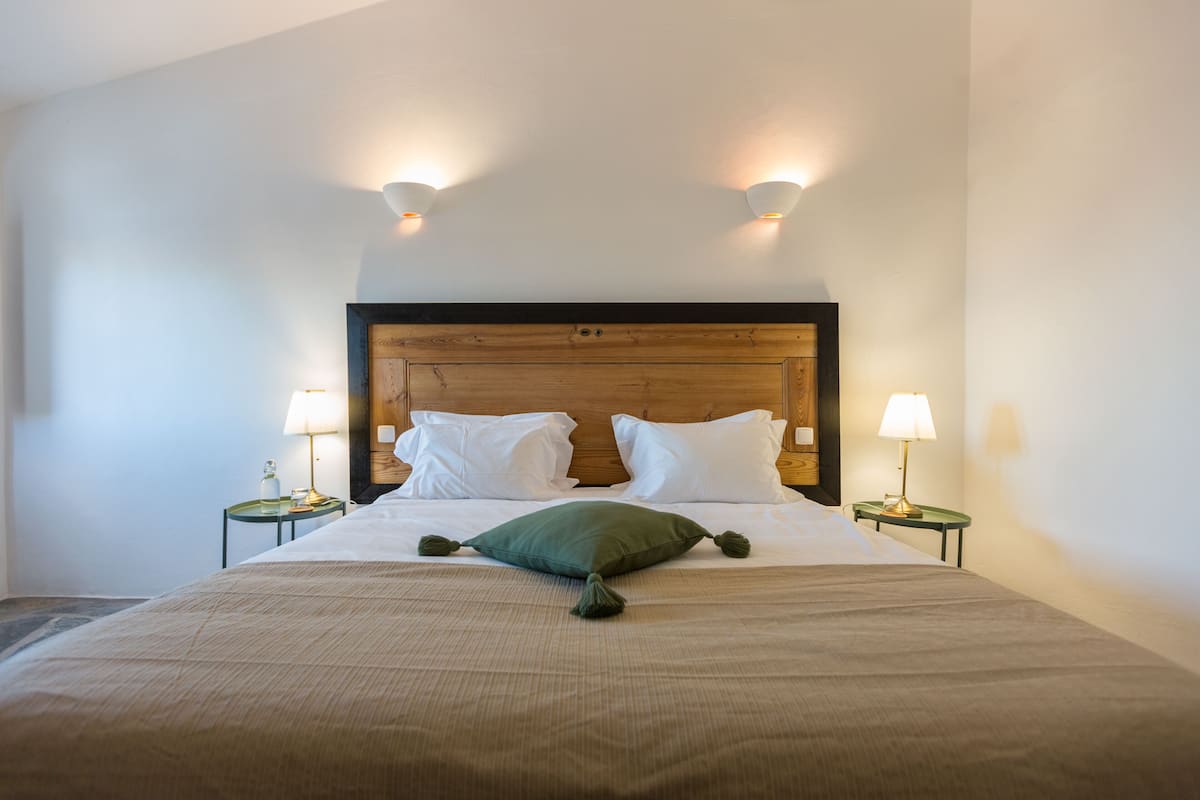 A neatly made bed with a wooden headboard, two bedside lamps, and a green pillow.