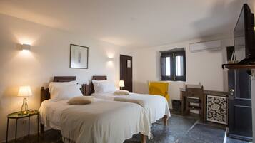 A hotel room with two beds, a small table with a lamp, a chair, a desk, and a fireplace.