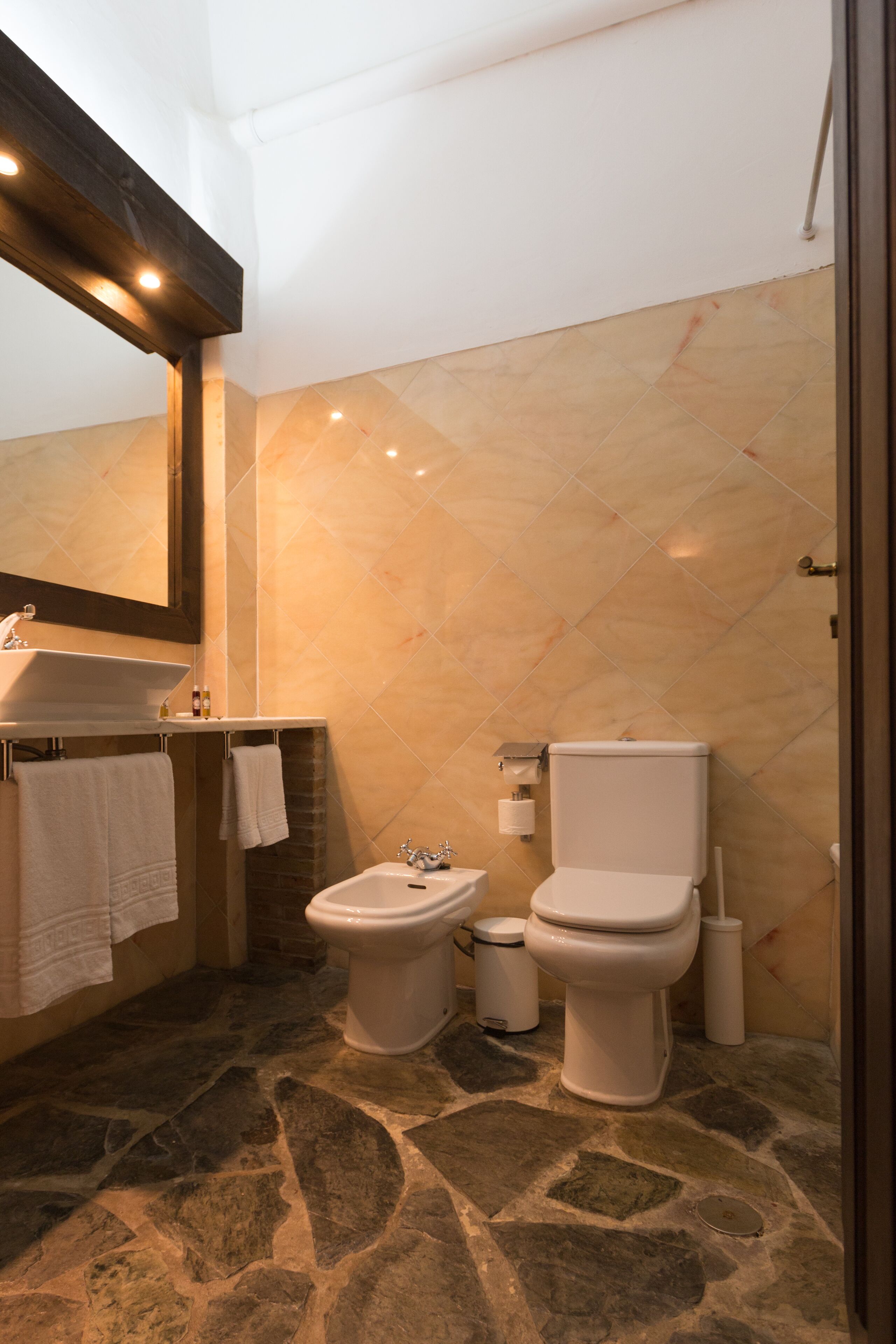 A bathroom with a stone floor, a sink, a bidet, and a toilet.