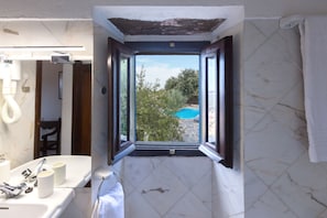 A bathroom with a window view of a swimming pool, a sink, and a mirror.