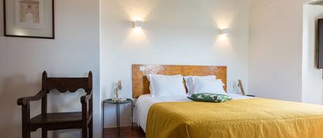 Un dormitorio con cama, una silla de madera, una mesita de noche y dos luces fijadas a la pared.