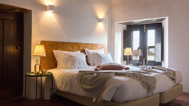 A bedroom with a bed, bedside lamps, a nightstand, and a window with a view.
