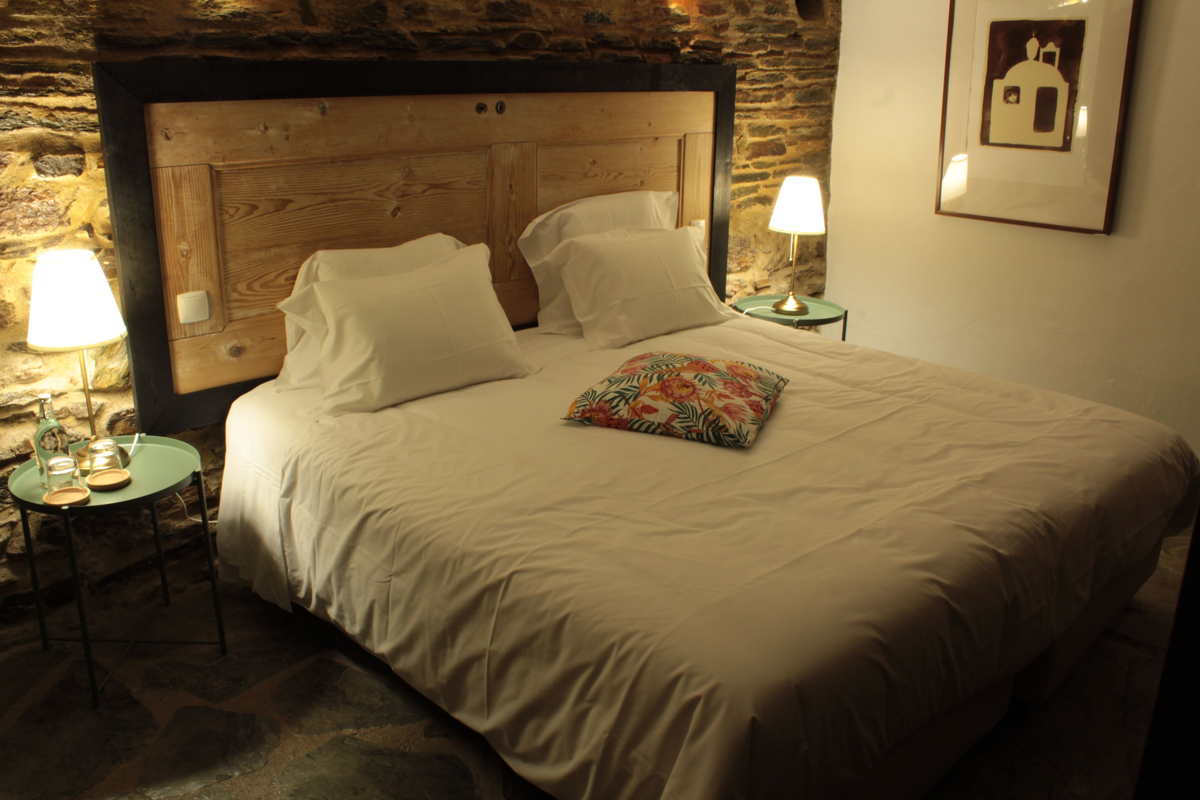 Un lit avec une tête de lit en bois, deux tables de chevet avec des lampes et un tableau encadré au mur.