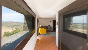 A corridor with a stone wall and a window overlooking a landscape. There is a yellow chair and a sofa in the room.