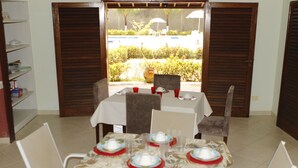 Un comedor con una mesa dispuesta para cuatro personas, sillas y vistas a una piscina y follaje exterior.