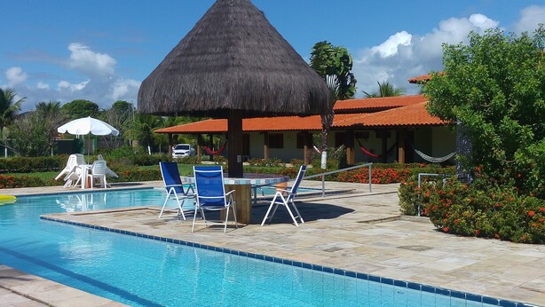 Una piscina con sillones de descanso y una estructura de techo de paja.