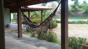 Un espacio al aire libre techado con una hamaca, piso de baldosas y una piscina al fondo.