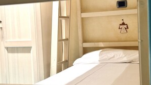 Un letto a castello con materasso bianco e un piccolo ripiano in legno con un ornamento appeso.