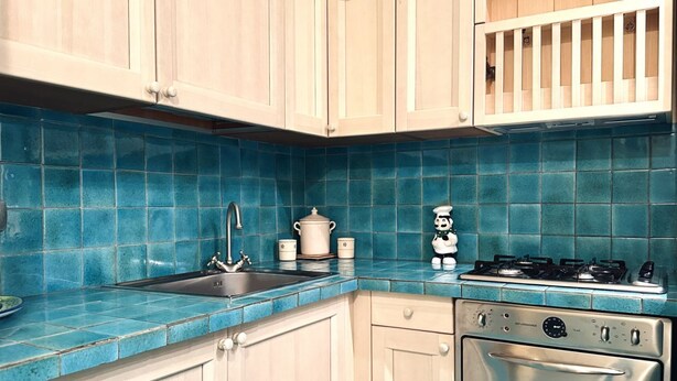 Una cucina con pensili in legno chiaro, zoccolo a mosaico blu, lavello in acciaio inossidabile, piano cottura e forno.