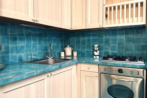 Une cuisine avec des meubles de couleur bois clair, un plan de travail bleu en carreaux, un évier en acier inoxydable, une cuisinière et un four.
