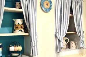 A room with striped curtains, a wall clock, shelves with decorative items, and a mug rack.