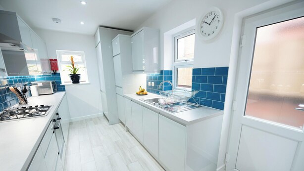 Una cocina moderna con armarios blancos, una estufa a gas, un lavadero con escurreplatos y un reloj en la pared.
