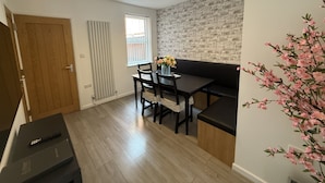 Una cocina moderna con suelo de madera, una mesa de comedor con sillas, encimera negra y pared decorativa de ladrillo.