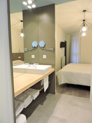 A modern bathroom with dual sinks, a large mirror, and a bed with a white bedspread. - Hotel Jacobeo (Burgos)