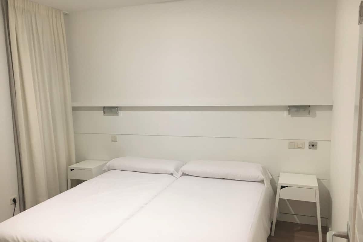 A hotel room with a double bed, two bedside tables, and a curtain.