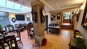 A spacious dining area with wooden tables and chairs, a stone pillar, and a kitchen area with cooking equipment. - Hotel Jacobeo (Burgos)