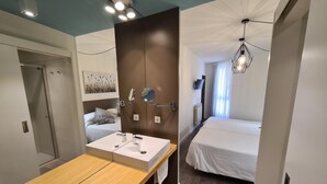 A modern bedroom with a wooden vanity, a bed, and a TV mounted on the wall. - Hotel Jacobeo (Burgos)