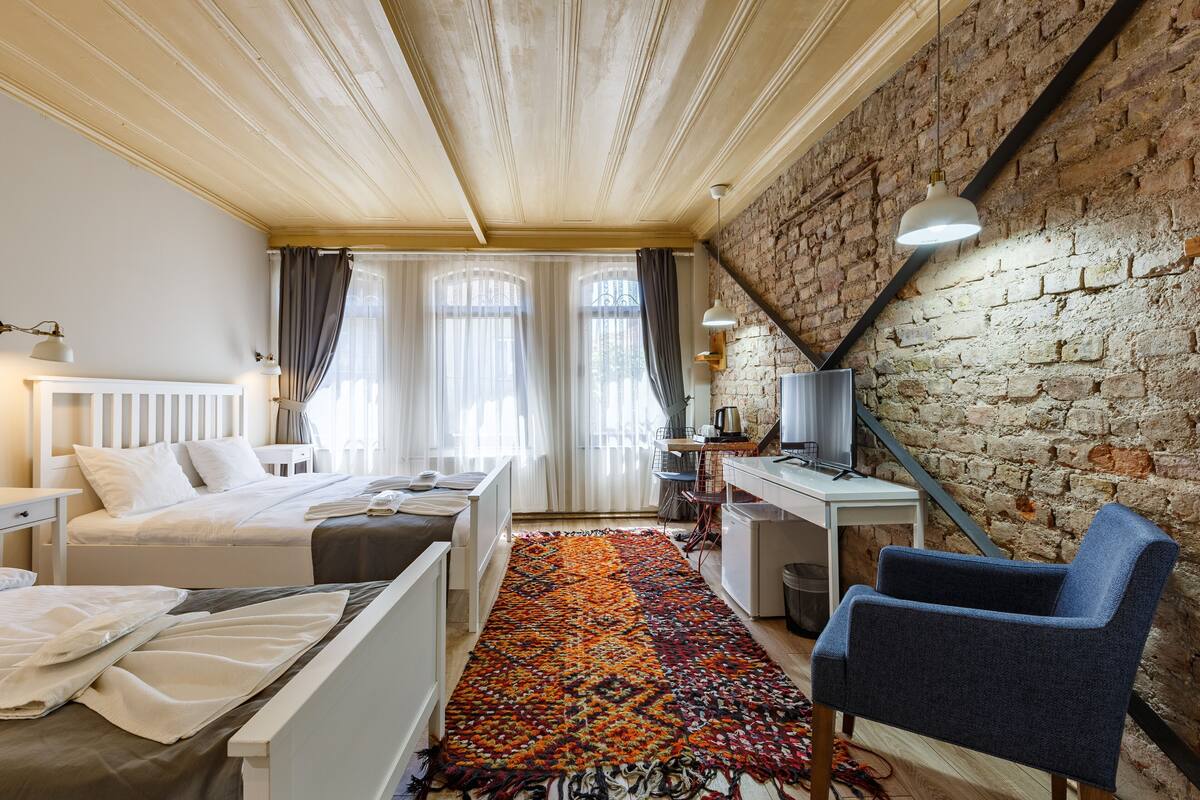 Una habitación de hotel con cama, escritorio, silla y una alfombra colorida.