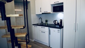 A compact kitchen with white cabinets, a microwave, a sink, and a coffee maker. - GOLDA apartments (Lodz)