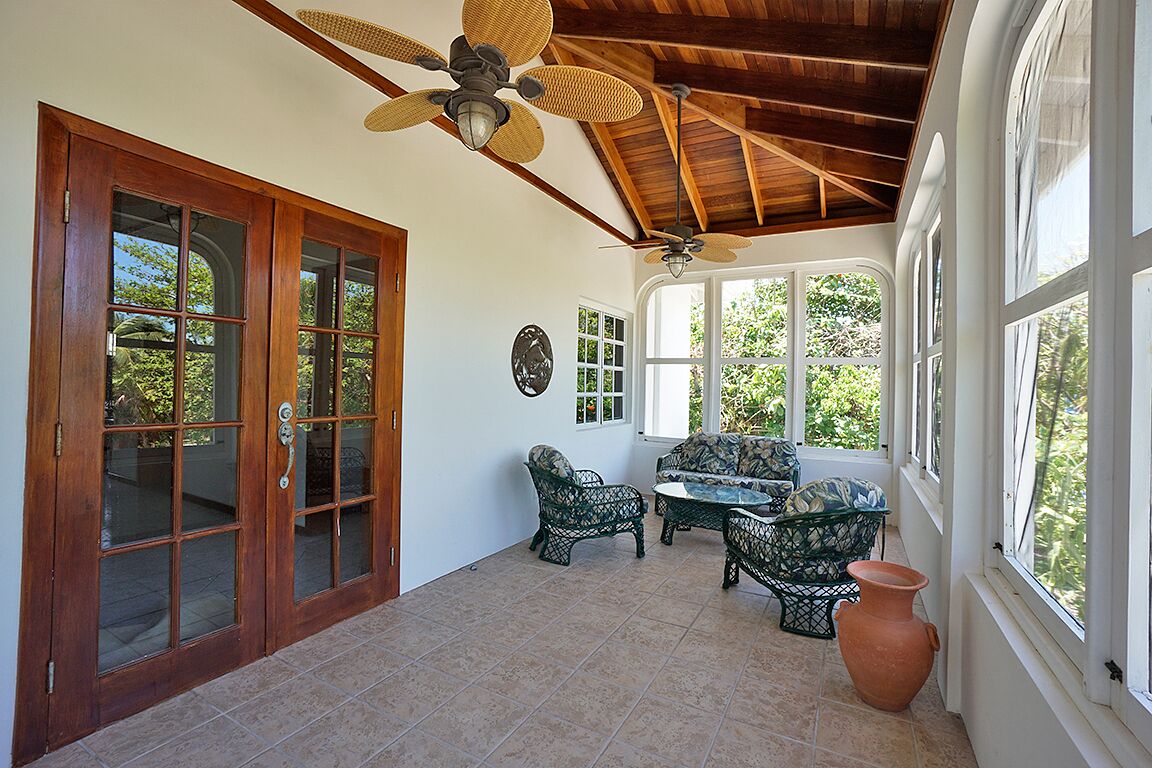 Un patio techado con un ventilador de techo, una puerta de madera y una zona de estar con mobiliario de mimbre.