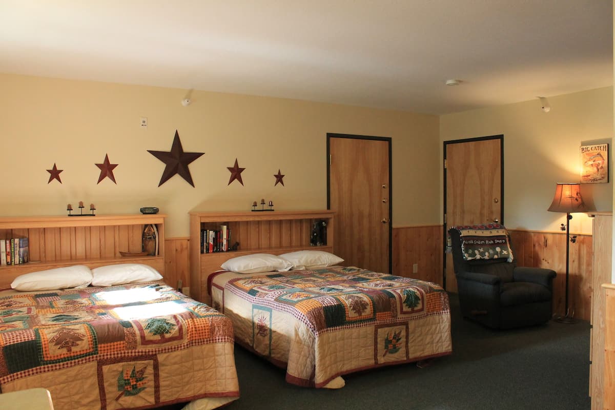A room with two beds, wooden headboards, a star decoration on the wall, a chair, and a lamp.