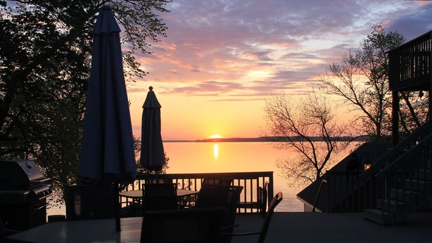 A patio with a table and chairs, overlooking a sunset over a body of water. - Viking Bay Resort & Lodge (Miltona)