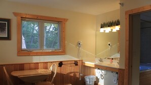 A bathroom with wooden paneling, a window with blinds, a sink, a mirror, and a heater. - Viking Bay Resort & Lodge (Miltona)