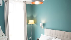 A neatly made bed with white linens and a striped blanket, a bedside lamp, and a wall-mounted light fixture in a room with teal walls and a white ceiling. - B&B BaRock (Noto)