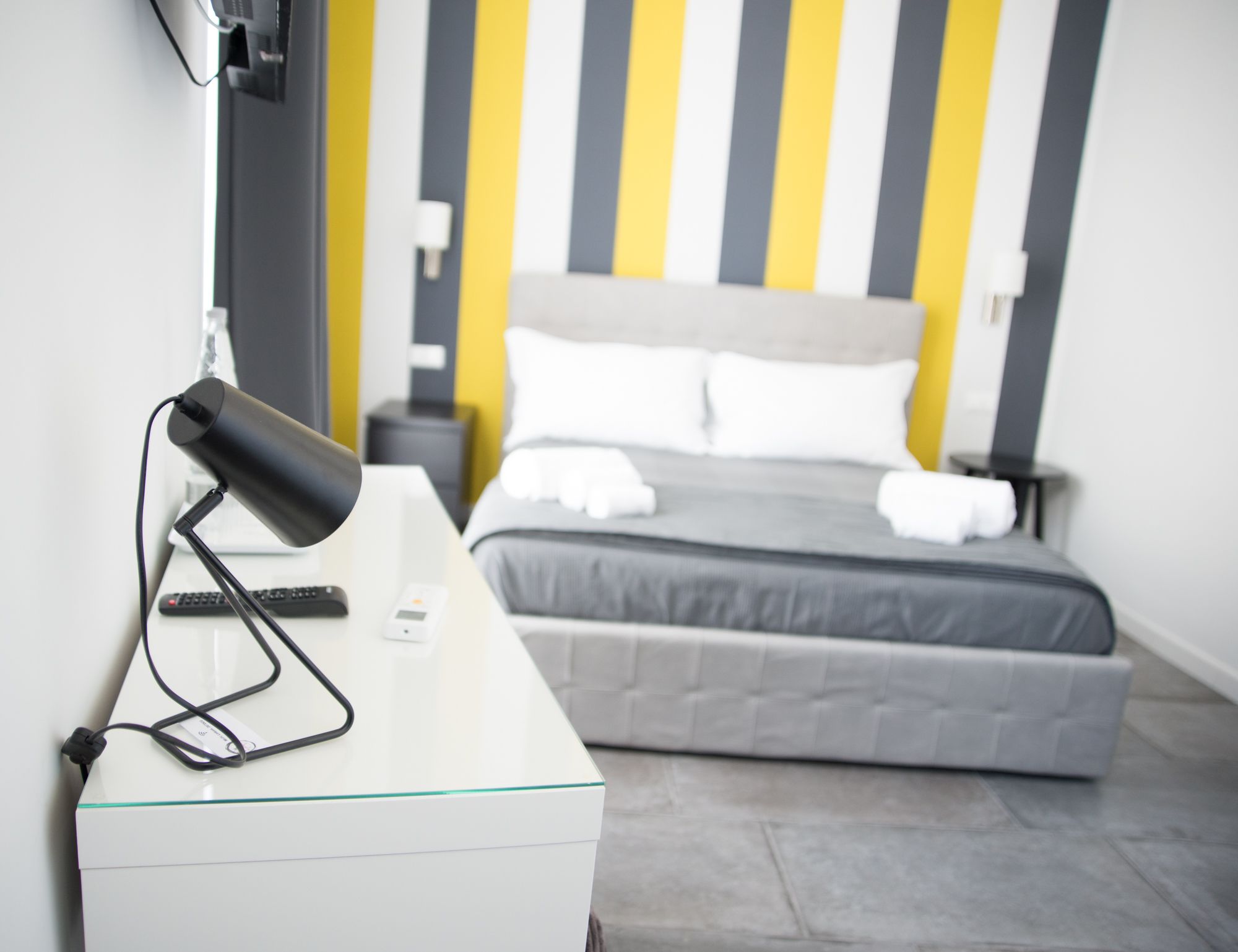 A hotel room with a bed, bedside table, lamp, and a wall-mounted TV.