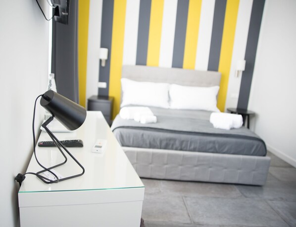Habitación de hotel con cama, mesita de noche, lámpara y televisor montado en la pared.
