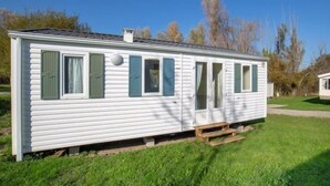 A single-story mobile home with a front door, two windows with shutters, and a small porch area. - Le Cabri Resort (Duras)