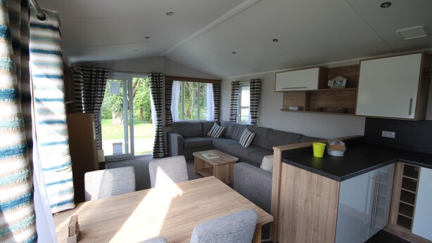 A modern RV interior with a dining area, sofa, kitchenette, and large windows. - Le Cabri Resort (Duras)