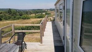 A wooden deck with a table and chairs, overlooking a rural landscape with fields and trees. - Le Cabri Resort (Duras)